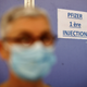 A woman wearing a protective face mask stands by a sign reading "Pfizer first injection" in a vaccination center in Antibes as part of the coronavirus disease vaccination campaign in France
